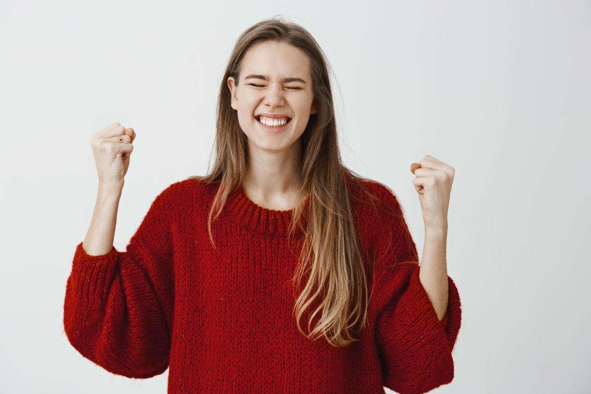 Mujer sonriente con jersey rojo celebrando con los puños levantados.